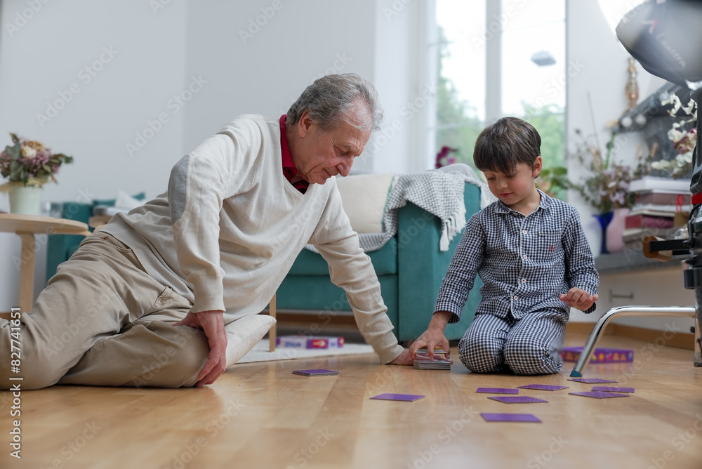 Elderly man and young boy playing card game on living room floor, boy ...