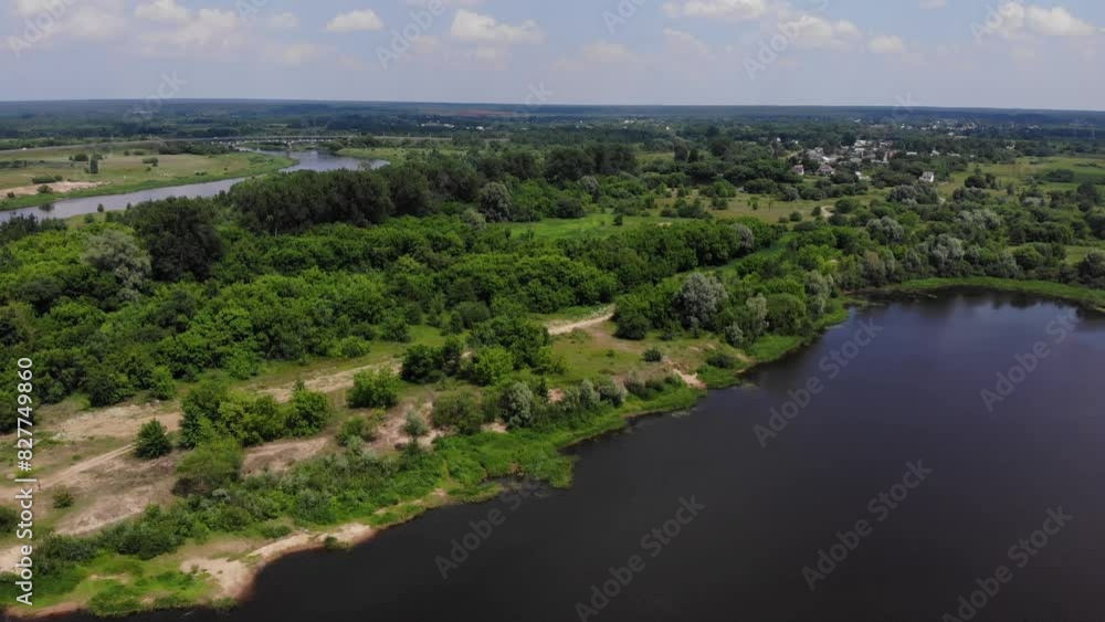 A scenic aerial view of a river surrounded by a lush forest, with a bridge and small village in the distance on a sunny day. A scenic aerial view of a river surrounded by a lush forest, with a bridge and small village in the distance on a sunny day.