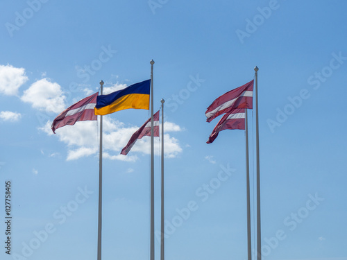 Latvian and Ukrainian flags on a blue sky background. Latvia's aid to Ukraine. Cooperation and friendship between countries