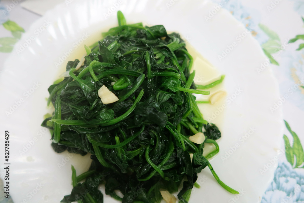 close up of homemade green spinach vegetables with garlic on a white plate and a table with blue flower white table cloth close up of homemade green spinach vegetables with garlic on a white plate and a table with blue flower white table cloth