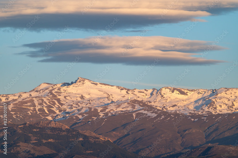 Huge lenticular clouds over the snowy peaks of the Sierra Nevada in Granada (Spain) at sunset