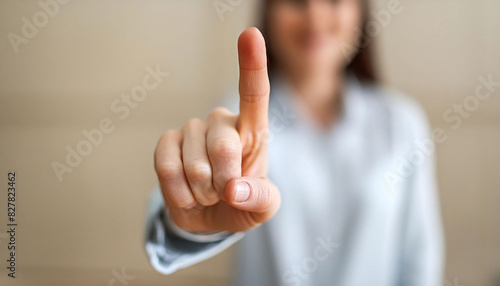 A woman with her index fingers upwards in focus, number one gesture, need for silence, be quite, with a softly blurred background. photo