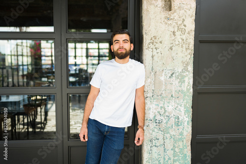 Confident young hispanic man poses in a white t-shirt mockup against a contrasting urban background