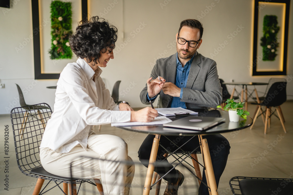 © Miljan Živković - Mature woman sign insurance or contract to adult man in cafe © Miljan Živković - Mature woman sign insurance or contract to adult man in cafe