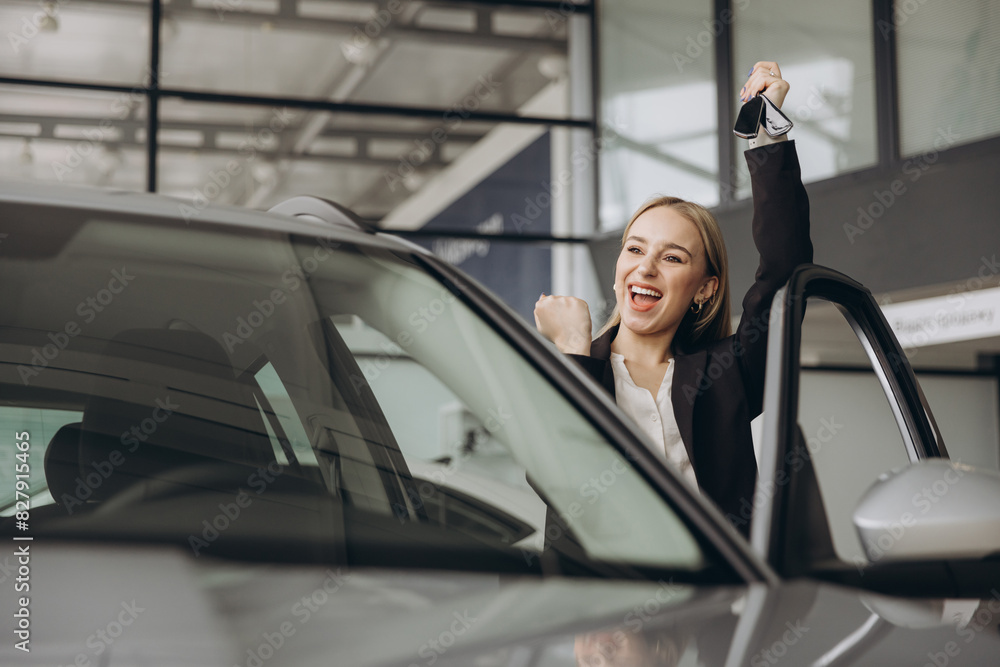 Cheerful woman standing near vehicle in dealership center and raising hands with excitement, copy space. Happy owner. Overjoyed Caucasian lady holding keys of new car after buying.
