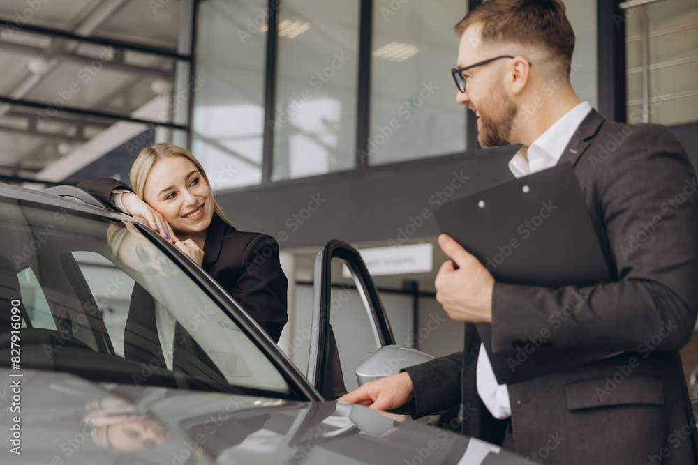 Beautiful young woman is talking to handsome car dealership worker while choosing a car in dealership Beautiful young woman is talking to handsome car dealership worker while choosing a car in dealership