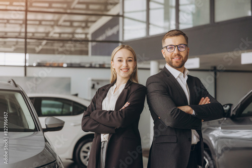 Smiling, friendly car sellers standing in car salon with arms crossed and announcing retail.