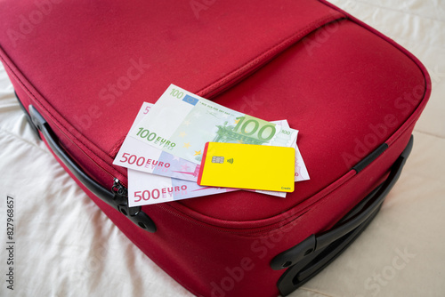 Euros and yellow credit card on a red suitcase on a bed