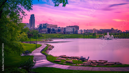 Fototapeta Naklejka Na Ścianę i Meble -  Omaha City Skyline at Sunrise over the Conagra Lake and vibrant green forest at the Heartland of America Park: The tranquil beauty of the midwestern metropolis in Nebraska