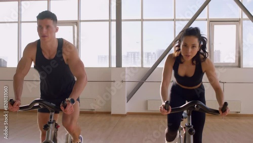 Athletic couple workout on static bicycle simulator, man trainer and fitness woman go in for sports together on bicycle simulators in the morning in bright room 4K B-Roll Footage