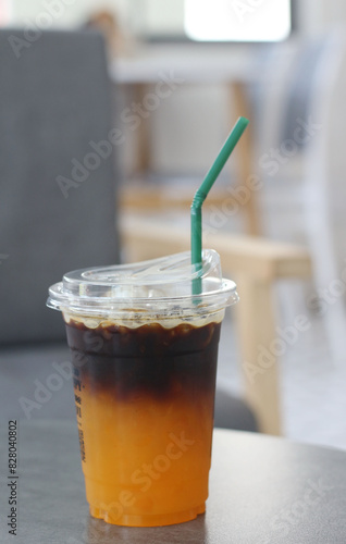 Iced Americano coffee with orange in plastic glass.Indoor cafe.