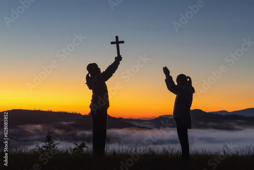 Silhouette two girls holding a holy cross praying on sunrise background, Crucifix, Symbol of Faith.