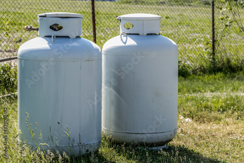 Two disconnected large vertical propane or LPG tanks resting in the grass at a construction site
