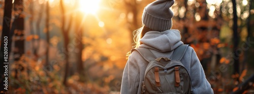 A young woman wearing an oversized hoodie and hat, carrying her backpack while walking in the forest, back view, autumn season. generative AI
