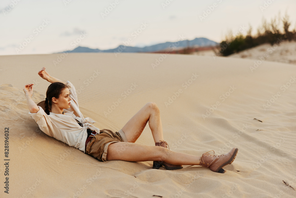 Woman laying on sand in desert with legs up in air under clear blue sky
