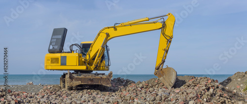 A yellow excavator working against a background of blue sky and sea