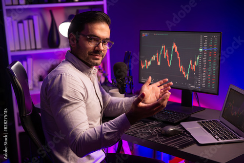 Profile of smart trader businessman looking camera analyzing in dynamic stock exchange investment on pc and laptop showing on screen with high profit in searching market at neon light office. Surmise. photo