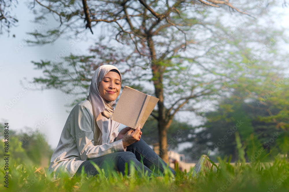 Smiling Asian Hijab Woman Reading Book Outdoors. Summer and outdoor concept while reading a book Smiling Asian Hijab Woman Reading Book Outdoors. Summer and outdoor concept while reading a book