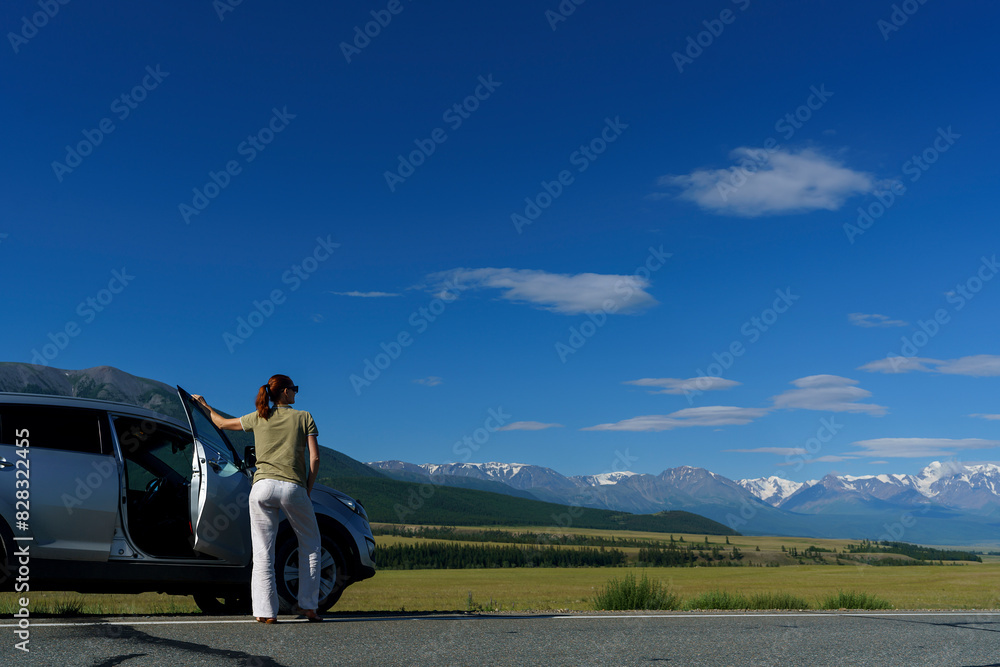 Obraz premium mature woman traveling by car stopped on the side of the road and admires the Altai mountains