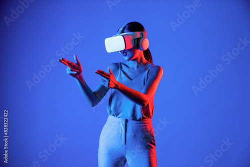 Smart female standing wearing VR headset connecting metaverse, future cyberspace community technology. Elegant woman using hands commanding virtual gun seriously playing shooting games. Hallucination.
