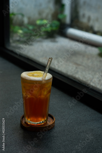 iced lemon tea drink served on transparent glass over small wooden plate on stone tile