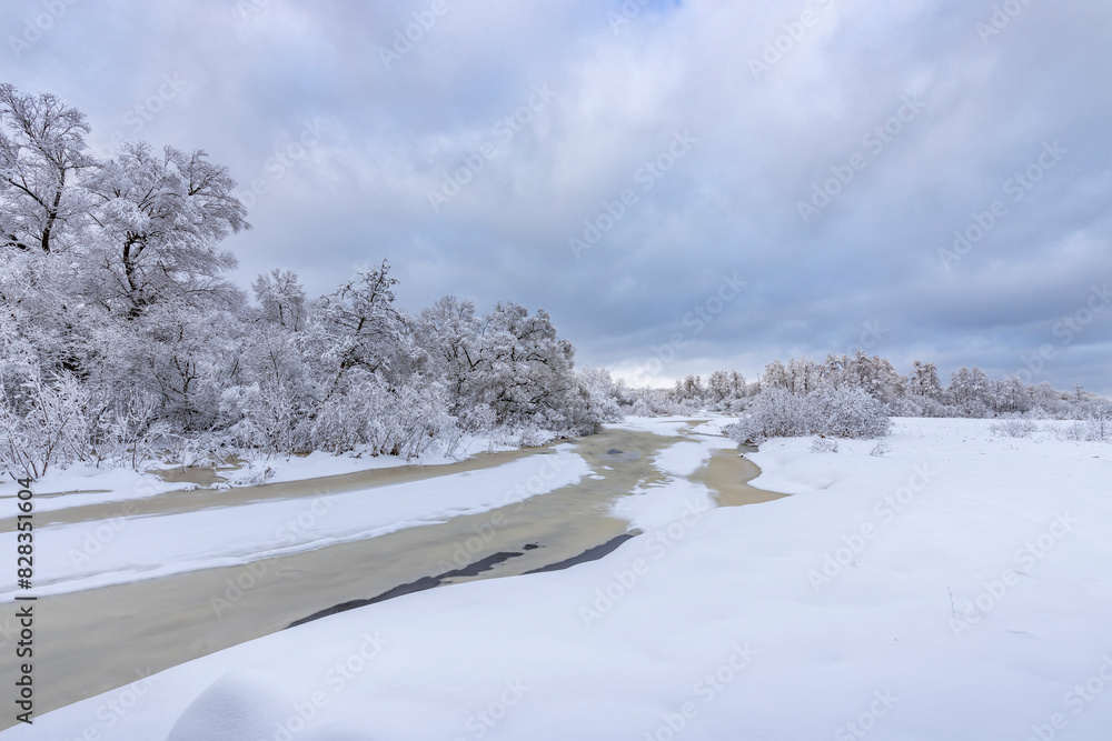 A serene snow-covered field envelops trees and a road, creating a beautiful winter scene. A serene snow-covered field envelops trees and a road, creating a beautiful winter scene.