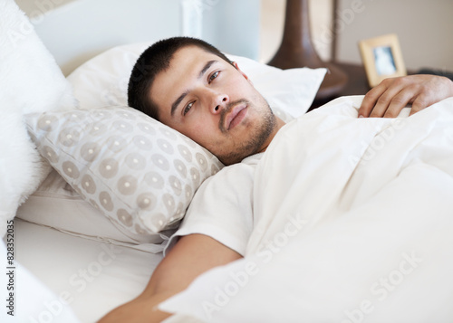 Morning, wake up and portrait of man in bed to relax with fresh start of new day in hotel room. Blanket, face and person in bedroom with rest, wellness and comfort in house, home or calm apartment.