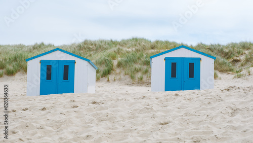 Two colorful beach huts with bright blue doors stand out against the sandy shore, creating a picturesque scene on the coast of Texel, Netherlands.