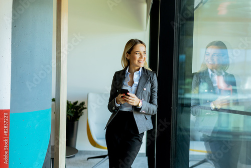 Businesswoman reading messages on smartphone in modern office, daytime reflection