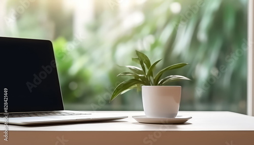 A laptop is on a table next to a plant and a cup
