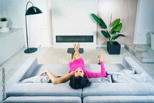 leggy charming brunette woman in a pink dress is resting on the sofa with a glass of champagne