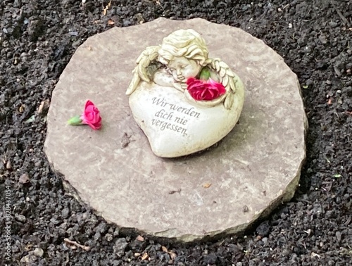 Herz mit Engel und Blumen auf dem Friedhof auf einem Grab mit Inschrift : Wir werden dich nie vergessen.  photo