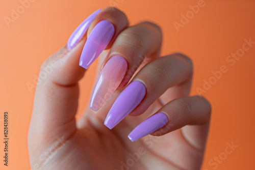 Photoof a woman's hand, the focus is on the nails, long pastel purple, elegant. Baby pastel background.The concept of femininity and care.