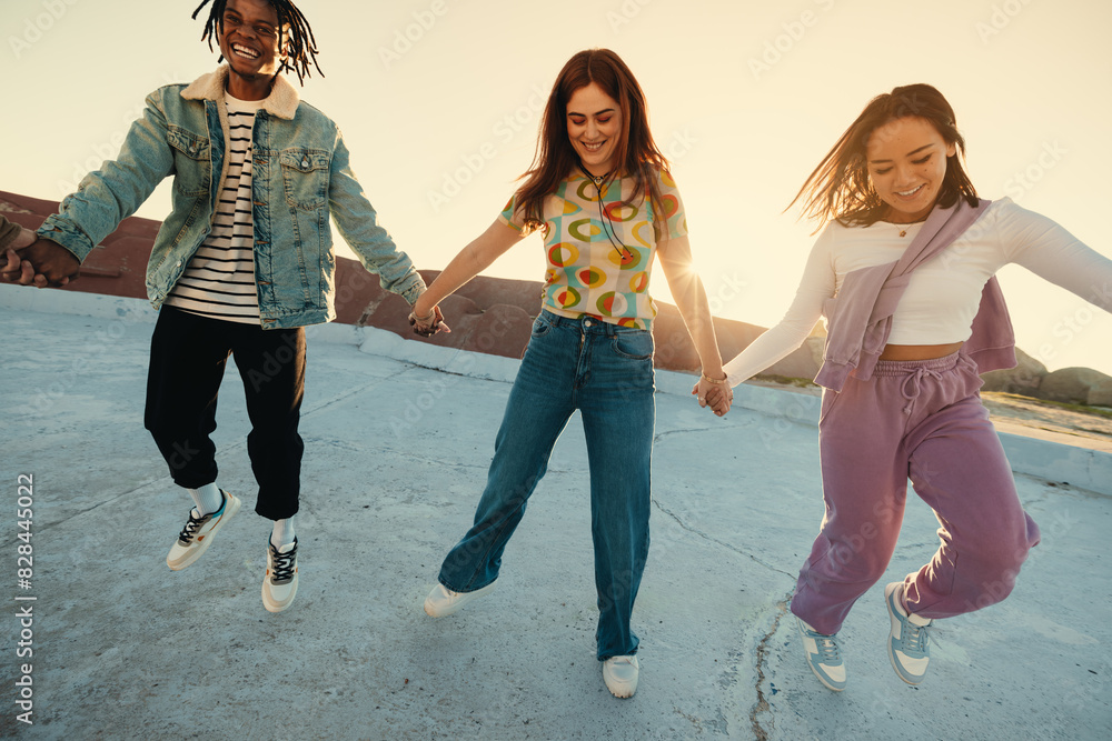 Fototapeta premium Happy friends holding hands and jumping on a sunny summer day outdoors