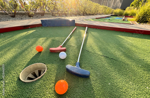 Assorted miniature golf putters and balls askew on synthetic grass.