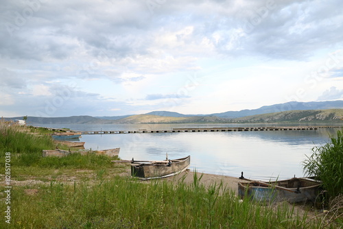 Boats anchored on shore at sunset by lake with mountain view