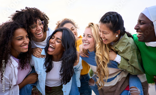 Large group of young different races only women friends standing having fun piggyback outdoors. Multiracial female laughing enjoying leisure time together. Generation z happy girls community people