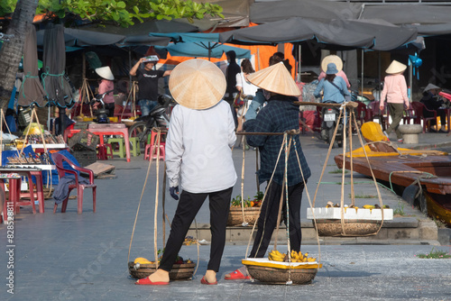 Vietnamese women sell fruits on the street of Hoi An ancient town on sunny day. Vietnam.