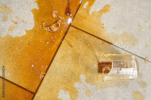 Shot of broken glass cup with poured coffee on tile floor