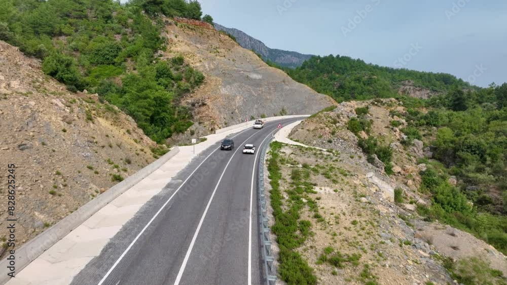 Aerial view of a white car driving on a highway through a mountainous landscape with rocky hillsides and green vegetation Aerial view of a white car driving on a highway through a mountainous landscape with rocky hillsides and green vegetation