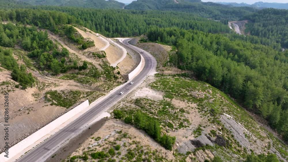 Aerial view of cars driving on a winding highway through steep, rocky mountainous terrain with sparse vegetation Aerial view of cars driving on a winding highway through steep, rocky mountainous terrain with sparse vegetation