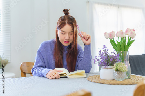 Asian business woman in sweater thinking to analyzing about strategy of business and writing business plan in notebook during planning about finance and market of new startup while working from home