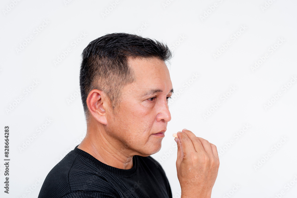 An asian man somberly takes a tablet for daily medication. Required to take for ailment or maintenance purposes. An asian man somberly takes a tablet for daily medication. Required to take for ailment or maintenance purposes.