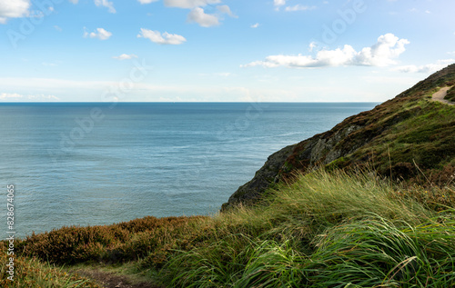 A cliff above the ocean on a sunny day, with water below and clouds in the sky