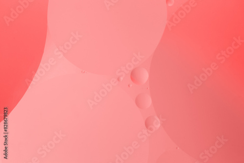Macro photography captures the symmetry of oil and water bubbles in shades of magenta, peach, and carmine on a pink background, forming a mesmerizing pattern of circles resembling delicate petals
