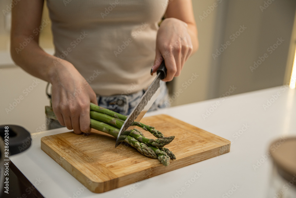 Caucasian girl cutting fresh asparagus on a wooden board in the kitchen Caucasian girl cutting fresh asparagus on a wooden board in the kitchen