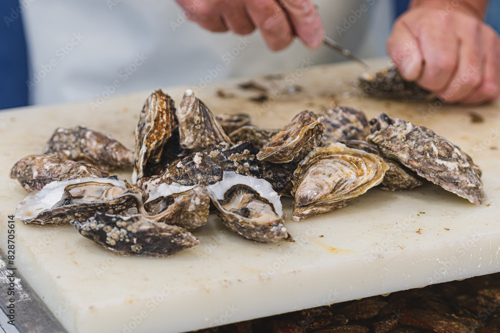 Seller opening oysters with a small knife in a fish shop or market, close up Seller opening oysters with a small knife in a fish shop or market, close up