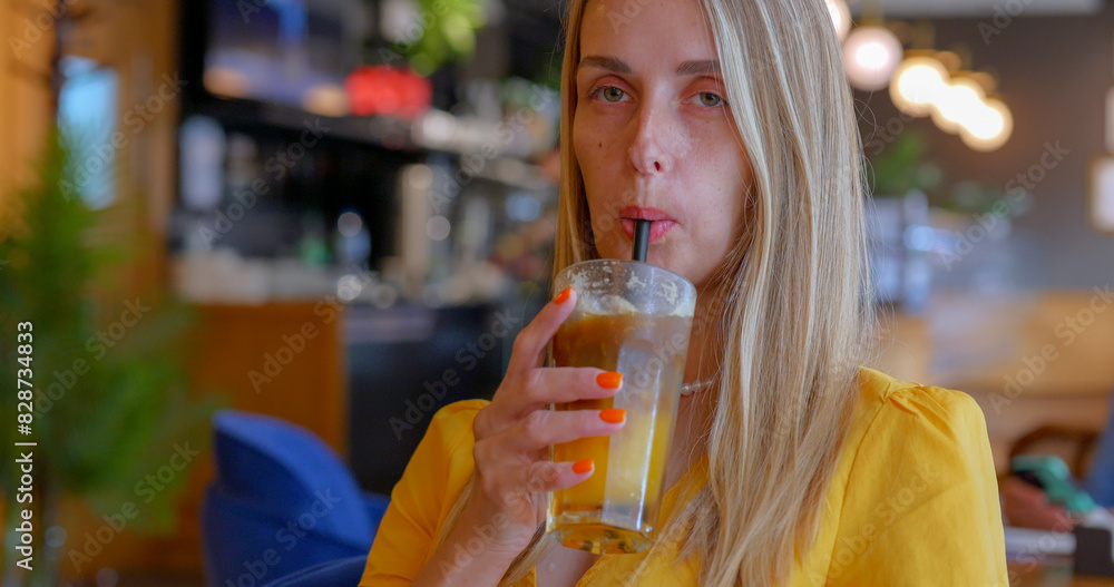 A blonde girl drinks iced coffee with orange juice in a cozy cafe A blonde girl drinks iced coffee with orange juice in a cozy cafe