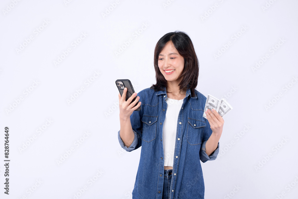 Asian woman wearing denim jean is holding dollar and a mobile phone against a white background, mobile banking concept. Asian woman wearing denim jean is holding dollar and a mobile phone against a white background, mobile banking concept.