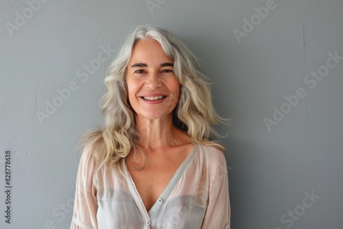 Cheerful mature woman poses against grey wall.